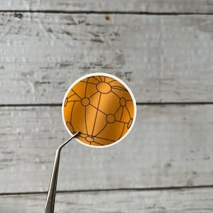 May include: A gold sticker with a black outline of a globe with connected lines and circles.