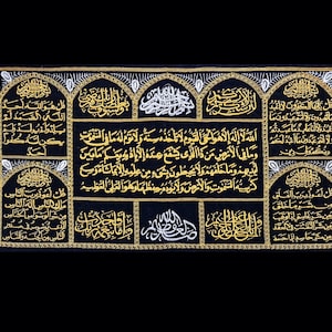 Könnte beinhalten: Ein schwarzer Wandbehang aus Stoff mit goldener Stickerei, die arabische Schrift in einem dekorativen Bogenmuster zeigt. Der Text enthält den Satz "Allah" und andere islamische Gebete.