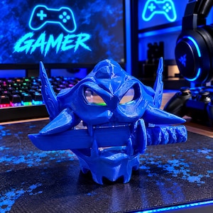 May include: A 3D-printed blue plastic figure of a stylized creature with pointed ears and a sharp, angular head. The creature has its mouth open, firmly gripping a horizontal katana sword between its teeth, showcasing a textured surface finish.