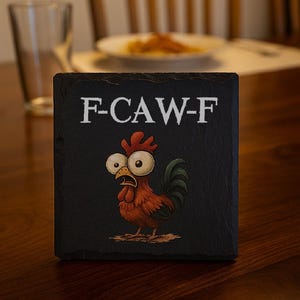 May include: Black square coaster with the text "F-CAW-F" in white. The coaster features a cartoon rooster with large eyes and a surprised expression. The rooster is primarily red and brown with a green tail.