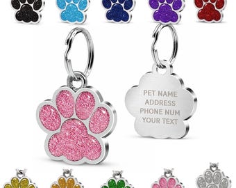 May include: A collection of paw print-shaped pet ID tags featuring a glittery finish in various colours including black, blue, purple, red, pink, gold, green, and silver. Each tag includes a metal split ring and a smooth back for custom engraving.