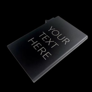 Puede incluir: Un objeto rectangular negro con el texto "YOUR TEXT HERE" en blanco. El objeto tiene una pequeña sección elevada en un lado. El fondo es negro.
