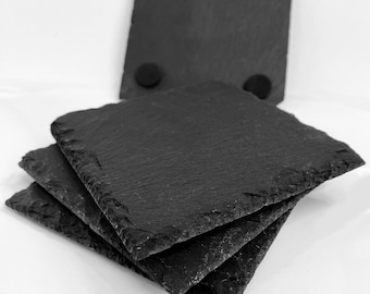 May include: Four black slate coasters with cork backing. The coasters are stacked on top of each other.