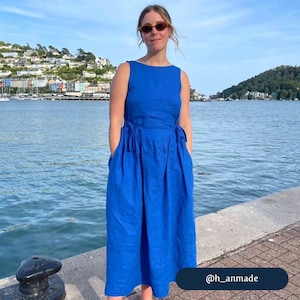 May include: A woman wearing sunglasses stands in front of a body of water wearing a bright blue sleeveless maxi dress with a tie at the waist. The dress has pockets on the sides. The text "@h_anmade" is visible in the lower right corner of the image.