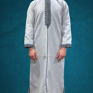 May include: A white hooded robe with a zipper closure and intricate black embroidery along the front and sleeves.