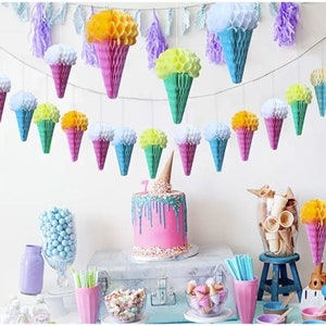 May include: A party table decorated with a honeycomb ice cream cone garland, a pink cake with sprinkles, and a variety of blue and white decorations. The table is set with a variety of snacks and drinks, including a bowl of blue candies, a glass of water, and a glass of juice.