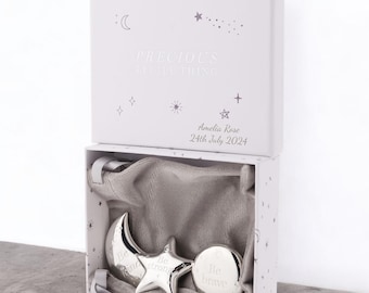 May include: A white gift box with a silver moon and star charm set. The box has a star pattern and the text "Precious Little Thing" and "Amelia Rose 24th July 2024". The charms are engraved with the words "Be strong" and "Be brave".