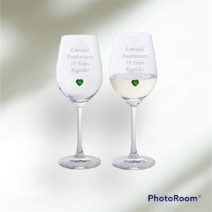 Pode incluir: Duas taças de vinho transparentes com pingentes em forma de coração verde esmeralda. As taças são gravadas com o texto "Emerald Anniversary 55 Years Together".