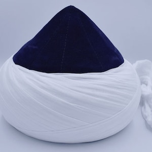 Peut inclure: Un turban traditionnel avec un sommet conique bleu foncé et une base blanche enveloppée. Une queue de tissu blanc s'étend sur le côté. Le turban est posé sur un fond uni.
