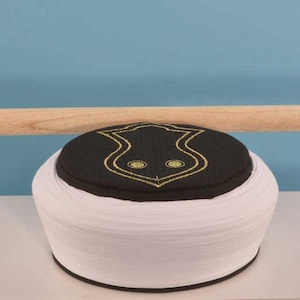 Könnte beinhalten: Eine weiße und schwarze Mütze mit einem goldenen Stickmuster. Die Mütze ist aus einem weichen, bequemen Stoff gefertigt und hat einen traditionellen Stil.