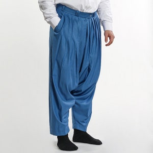 Puede incluir: Un pantalón azul plisado con un corte holgado y amplio. El pantalón está hecho de una tela lisa y antiarrugas.