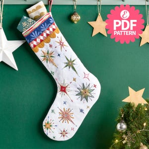 May include: White Christmas stocking with embroidered starburst designs in various colors. The top of the stocking features a decorative band with blue, red, and gold patterns. The stocking is filled with small gifts and is hanging on a green wall.