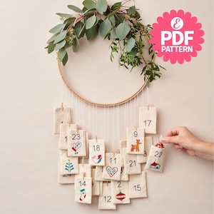 Puede incluir: Un calendario de adviento navideño hecho a mano con 24 bolsitas de tela numeradas que cuelgan de un aro de madera decorado con vegetación. Cada bolsita presenta un diseño navideño bordado diferente, como un reno, una media y un árbol de Navidad.