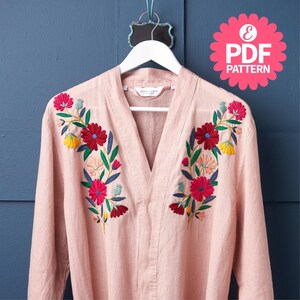 May include: A light pink long-sleeved shirt with a V-neck, adorned with colorful floral embroidery. The embroidery features red, yellow, and pink flowers with green leaves. The shirt hangs on a white hanger against a blue background. A pink "PDF PATTERN" graphic is in the upper right.