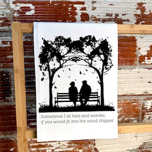 May include: White kitchen towel with a black silhouette of two people sitting on a bench under trees. The text reads, "Sometimes I sit here and wonder, if you would fit into the wood chipper."