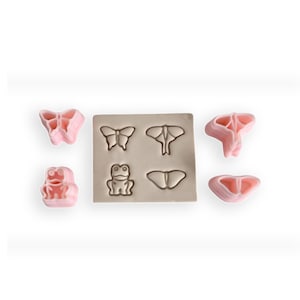 May include: A set of pink silicone moulds for making fondant or gum paste decorations. The moulds feature butterfly and frog designs.