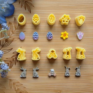May include: A set of 14 yellow plastic cookie cutters in various Easter-themed shapes, including eggs, bunnies, flowers, and paw prints. There are also two sets of smaller, grey plastic bunny cookie cutters.