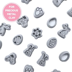 May include: An assortment of grey metal clay moulds in shapes such as a paw print, flower, egg, and rabbit. The moulds are arranged on a white backdrop. A pink circle with the text "FOR PRECIOUS METAL CLAY" is in the upper left corner.