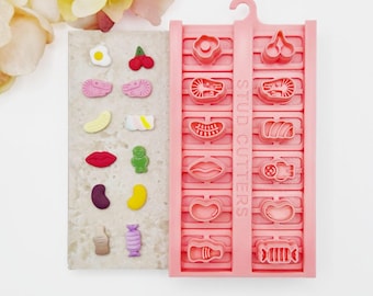 May include: A pink plastic mold tray labeled STUD CUTTERS with twelve distinct shapes for creating small items. Beside the tray, twelve corresponding miniature figures are displayed, including a fried egg, cherries, lips, a candy, and a bottle.