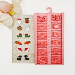 May include: A pink plastic mould with the text STUD CUTTERS featuring various holiday shapes alongside a beige display card with matching miniature clay pieces including Santa, reindeer, elf shoes, carrots, hats, and boots in festive colours.