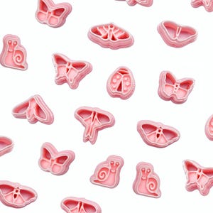 May include: A collection of pink plastic cookie cutters in the shapes of insects and animals, such as butterflies, snails, and ladybirds. The cutters are arranged on a white background. Suitable for baking and crafts.