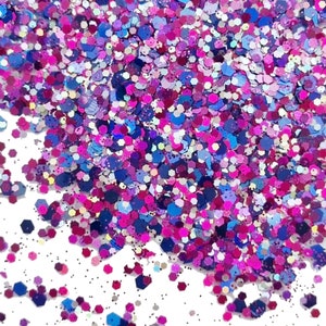 May include: A close-up of a pile of iridescent glitter in shades of pink, purple, and blue. The glitter is scattered on a white surface.