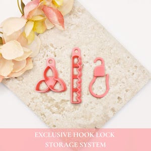 May include: Three pink plastic tools for an exclusive hook lock storage system. The set includes a triangular three-lobed piece, a rectangular strip with five wavy cutouts, and a single hook-shaped component, all featuring small circular holes.