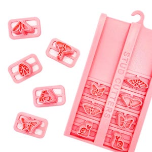 May include: A set of pink plastic stud cutters featuring various insect and animal shapes including butterflies, a ladybug, and a snail. The set includes a rectangular storage tray with the text STUD CUTTERS embossed vertically on the side.
