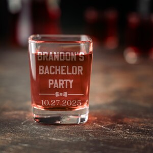 Puede incluir: Un vaso de chupito de vidrio transparente lleno de un l&iacute;quido rojo. El vaso est&aacute; grabado con el texto "Brandon's Bachelor Party" y la fecha "10.27.2025". Tambi&eacute;n hay un peque&ntilde;o gr&aacute;fico de corbata de lazo grabado en el vaso.