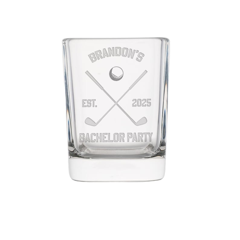 May include: Clear glass shot glass with etched golf-themed design. The design includes crossed golf clubs, a golf ball, and the text "Brandon's", "EST. 2025", and "BACHELOR PARTY".