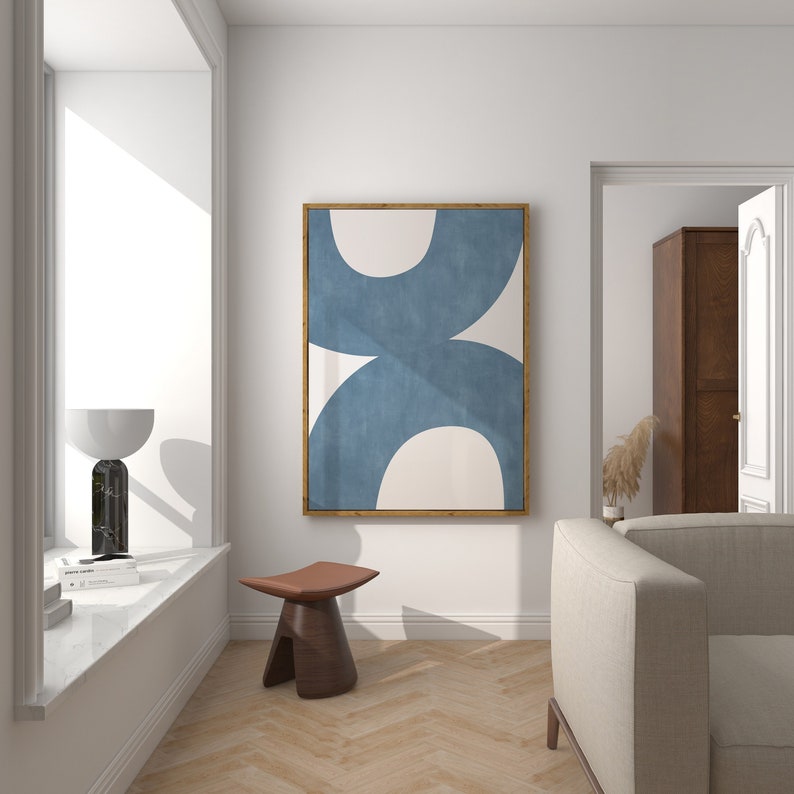 May include: A modern living room interior with a white wall, a wooden floor, a white couch, a wooden stool, and a framed abstract painting with blue and white shapes.