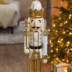 May include: A white and gold nutcracker with a crown, mustache, and beard. The nutcracker is holding a gold staff with a fleur-de-lis on top. The nutcracker is standing on a gold base.