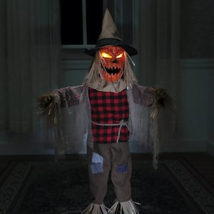 May include: A spooky scarecrow with a pumpkin head and glowing eyes, wearing a plaid shirt, brown pants, and a witch's hat. The scarecrow is standing on a rug with a patterned design.