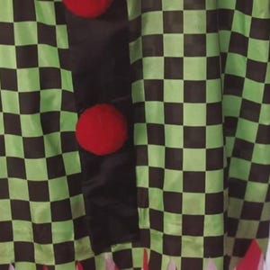 May include: A costume featuring a green and black checkered pattern. The costume has three large red pom-pom buttons down the front. The bottom of the costume has red fringe.