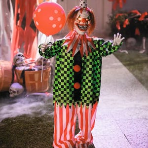 May include: A Halloween clown decoration with a menacing expression. The clown wears a green and black checkered jacket, red and white striped pants, and holds an orange balloon with white polka dots. The clown has red hair and a polka-dot hat.