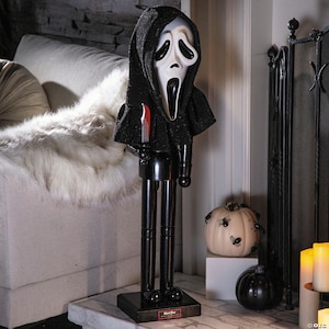 May include: A Halloween-themed nutcracker figure of Ghostface, with a white mask and black hooded cloak, holding a small knife. The figure has black legs and a black base with the text "Ghost Face".
