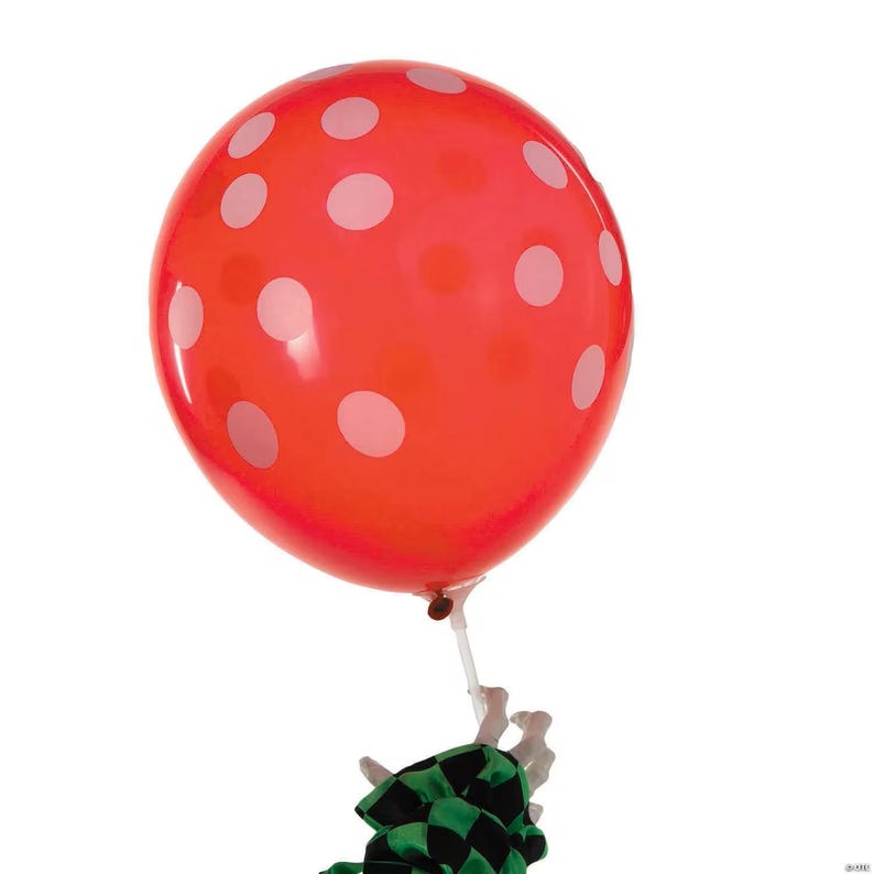 May include: A large red balloon with white polka dots. The balloon is tied to a white stick and a green and black checkered ribbon. The balloon is inflated and appears to be floating against a white background.