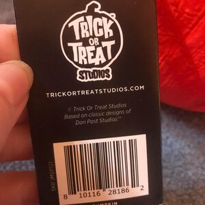 May include: A black tag with the text "TRICK OR TREAT STUDIOS" in a white circular logo. The tag also includes the text "DEVELOPED BY JUSTIN MABRY" and a barcode. The word "PUMPKIN" is printed at the bottom of the tag.
