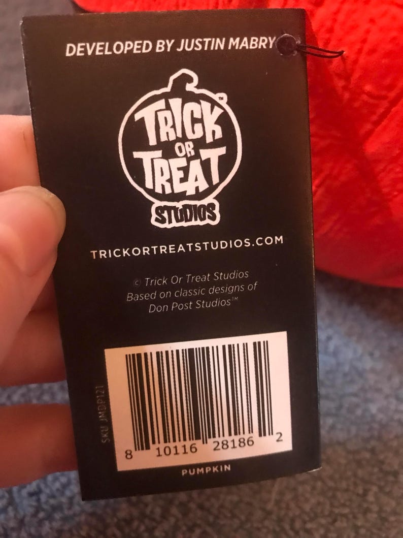 May include: A black tag with the text "TRICK OR TREAT STUDIOS" in a white circular logo. The tag also includes the text "DEVELOPED BY JUSTIN MABRY" and a barcode. The word "PUMPKIN" is printed at the bottom of the tag.
