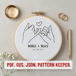 May include: A circular wooden embroidery hoop containing white Aida fabric with a black line art design of two hands pinky promising under a heart. The text reads MIKE & MAY 12 | 05 | 27. Below the hoop, text reads PDF. OXS. JSON. PATTERN KEEPER.