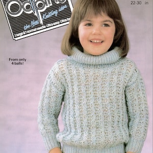 May include: A child wearing a light blue knitted turtleneck sweater. The sweater has a textured pattern and long sleeves. The image includes text for a knitting pattern, with measurements of 22-30 inches.