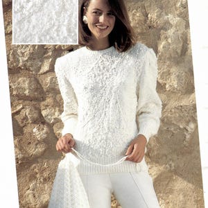 May include: A woman wearing a white knit sweater with a textured pattern, matching pants, and a drawstring bag. The sweater has a crew neck and long sleeves. The image also shows a close-up of the knit texture. The text "A365" is visible.