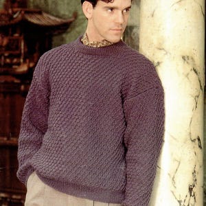 May include: A dark purple, textured knit sweater with a crew neck. The sweater has a diamond pattern and is paired with light brown pants. The image includes the text "JAEGER DOUBLE KNITTING" and measurements of 32-46 inches.
