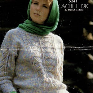 May include: A woman wearing a green scarf and a light blue sweater with a cable knit pattern. The sweater is 30-44 inches (76-112 cm) in size. The image is from a knitting pattern book.