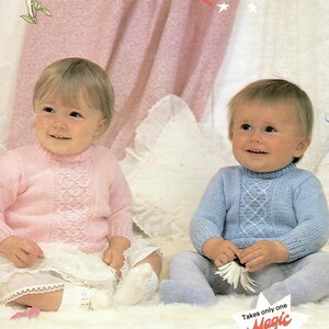May include: Two babies wearing knitted sweaters. The baby on the left is wearing a pink sweater with a white lace trim. The baby on the right is wearing a blue sweater. The sweaters have a diamond pattern. The text "Patons FAIRYTALE DK" is visible in the background. The text "Takes only one Magic Value 100g ball." is also visible in the background.