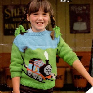 Puede incluir: Un suéter de punto verde, azul y blanco con un diseño de Thomas la locomotora. El suéter es para un niño y tiene cuello redondo. El suéter mide 51-66 cm.