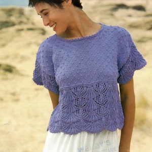May include: A purple knitted top with a lace pattern and a round neckline. The top has short sleeves and a textured design.