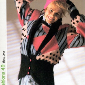 May include: A woman wearing a black, pink, and blue patterned sweater with black polka dots. The sweater has a black, fuzzy collar and a pink hat. The woman is wearing black pants and a light blue shirt.