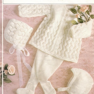 May include: A white knitted baby outfit set, including a cardigan, a bonnet, and leggings. The set is made with a double knitting technique and features a cable stitch pattern. The outfit is suitable for babies aged 18-20 inches.