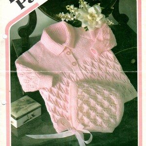 May include: A pink knitted baby cardigan and matching hat set with a white ribbon. The pattern is a delicate lace stitch. The set is made with Darling 3 ply yarn and is a Wendy design.